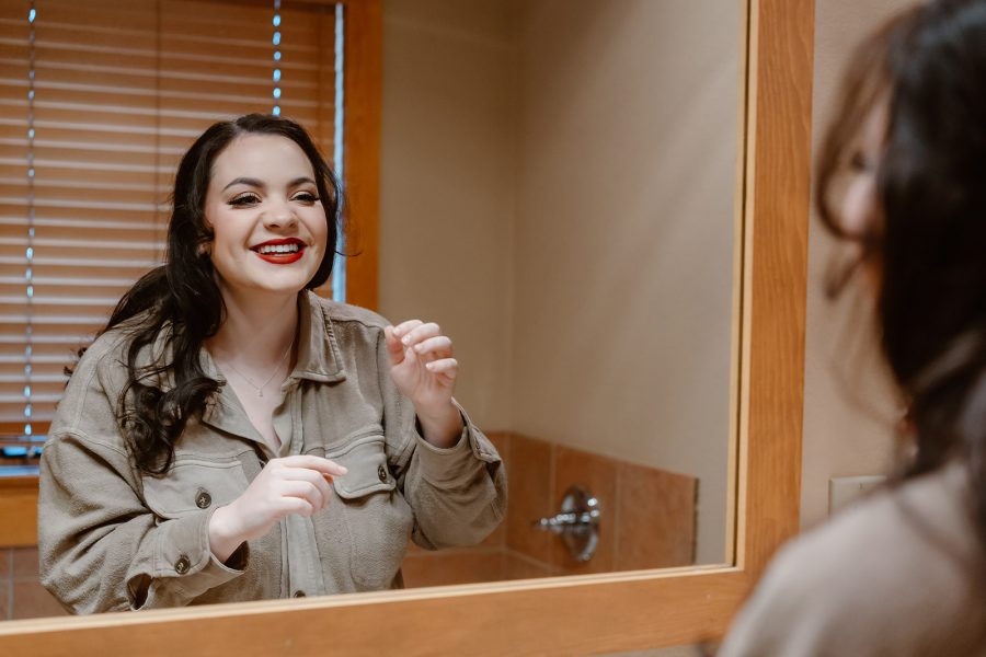 A bride smiles at herself in the mirror as she gets ready for her Breckenridge winter elopement. 