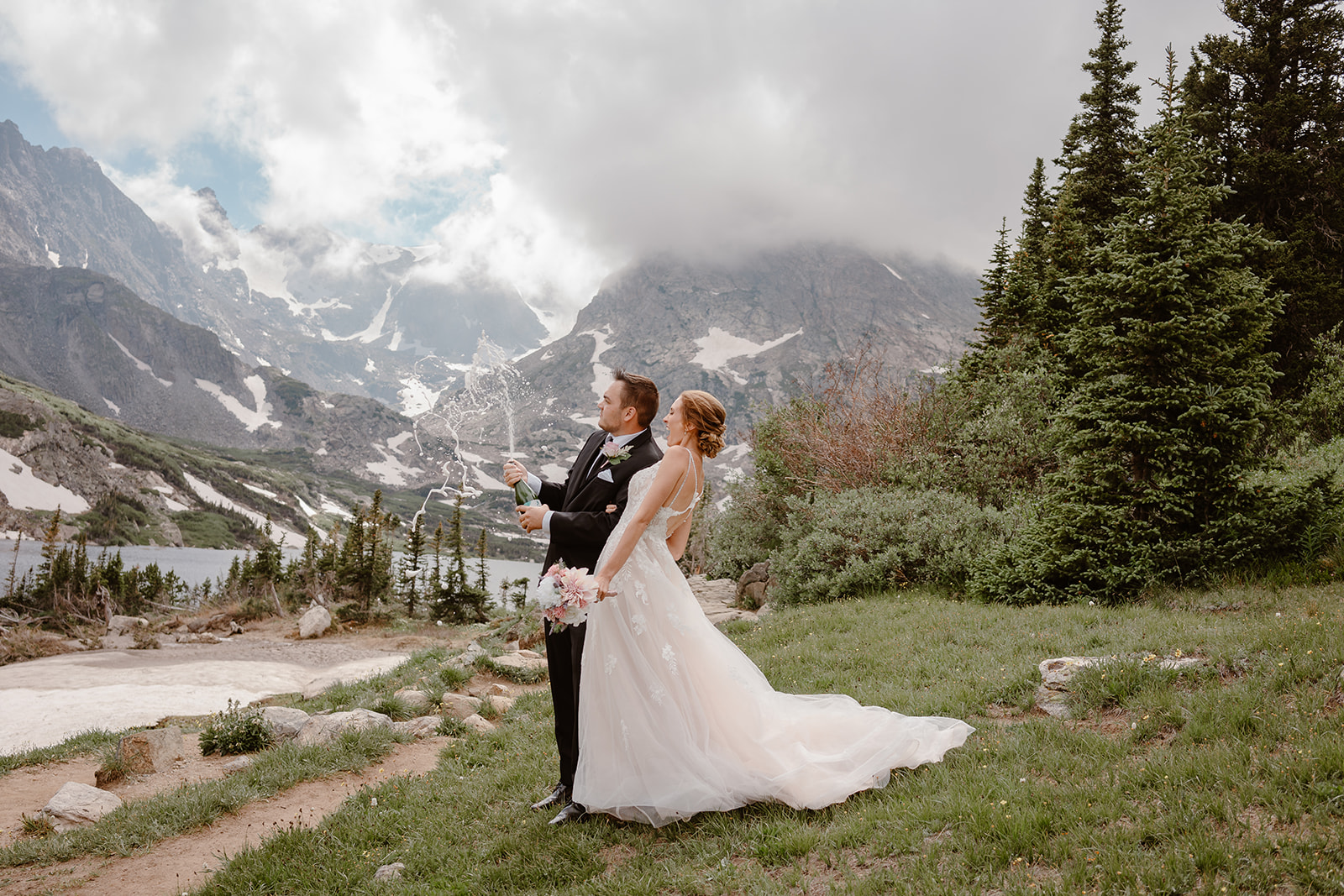 A couple pops champagne during their hiking elopement in Lake Isabelle.