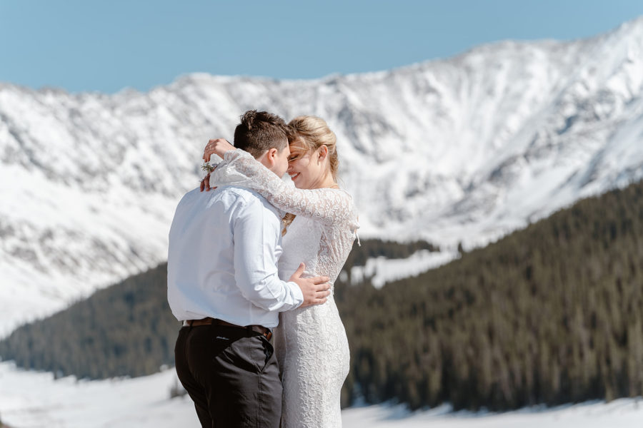 The bride and groom hold each other close in front of a beautiful mountain peak during their Breckenridge spring elopement.