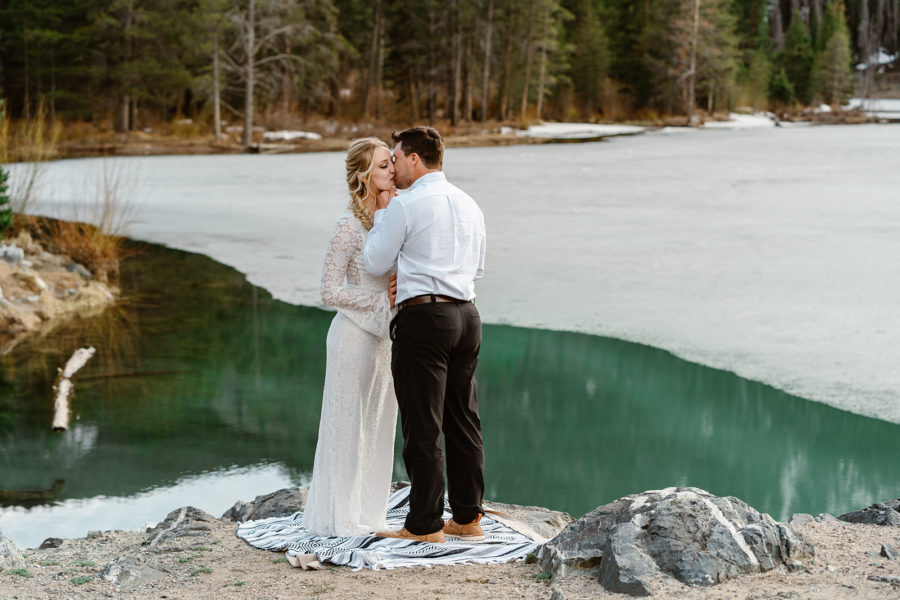 A bride and groom kiss each other in front of a frozen, alpine lake in Breckenridge, Colorado, during their adventure elopement.