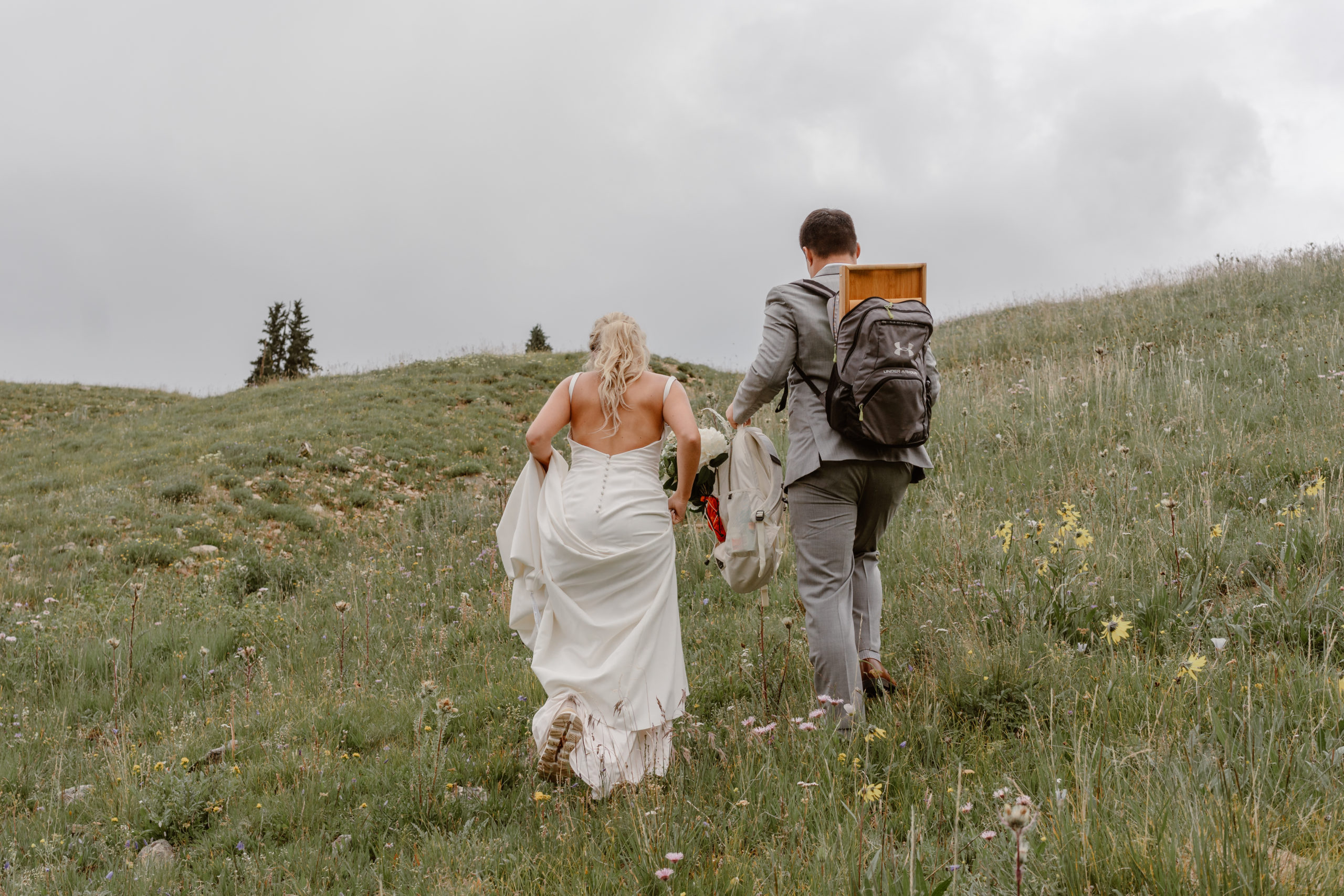 A bride and groom scramble up a Colorado mountain wearing their wedding attire during their Colorado mountain elopement. 