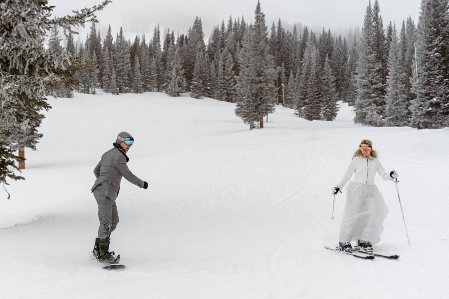 A bride and groom carve down the mountain on their skis and snowboard during their Breckenridge Ski Resort wedding.