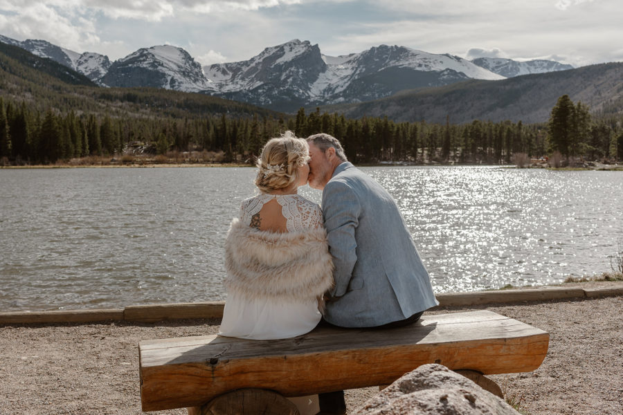 A bride and groom kiss at an overlook as they experience their wedding day at Sprague Lake.