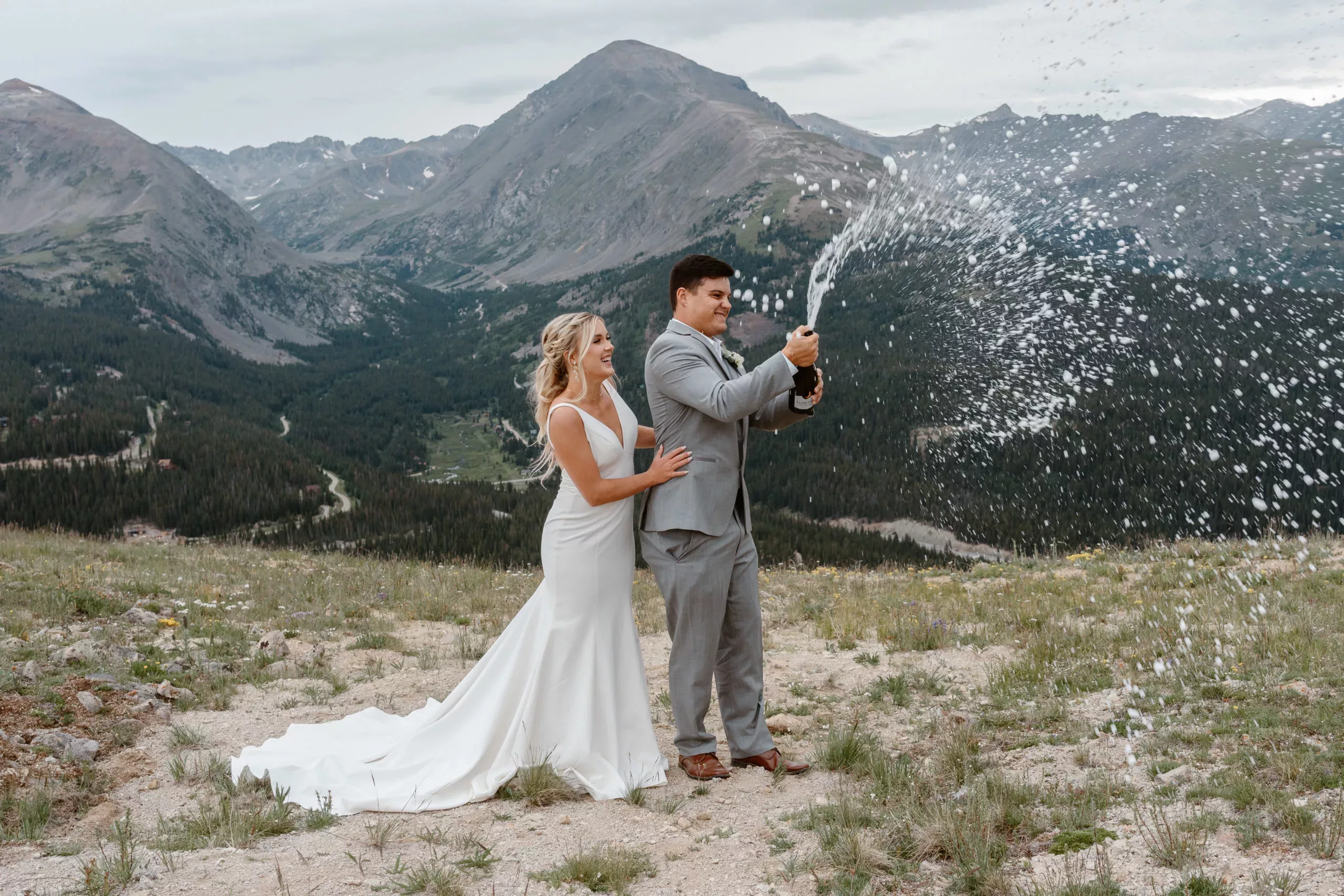 A bride and groom pop champagne at the top of a Colorado mountain during their Sapphire Point wedding.