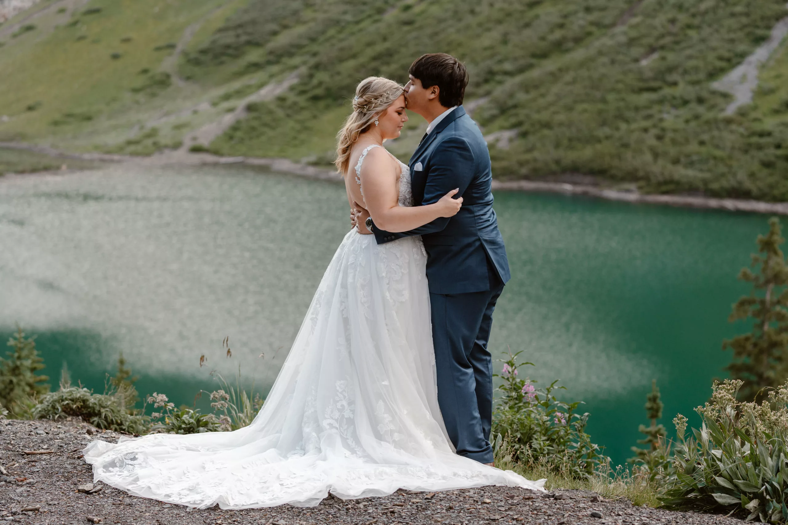 A bride and groom hold each other close as they kiss in front of a stunning alpine lake during their summer Crested Butte elopement.