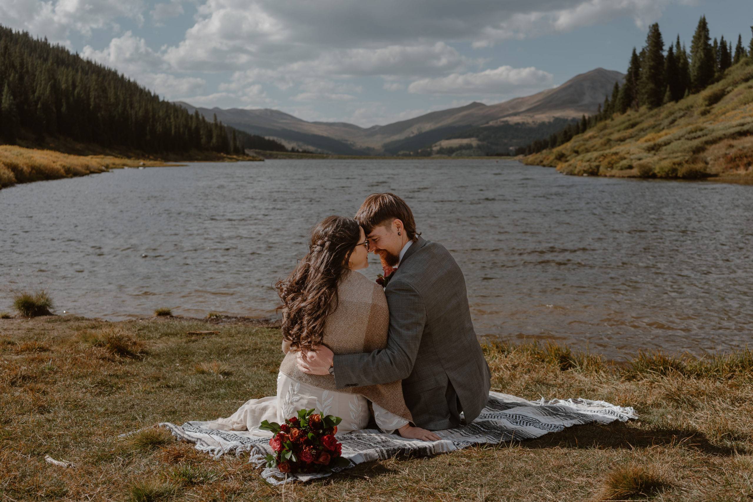 Sitting on a blanket, a bride and groom soak in the mountain views of their wedding day during their Breckenridge mountain elopement.