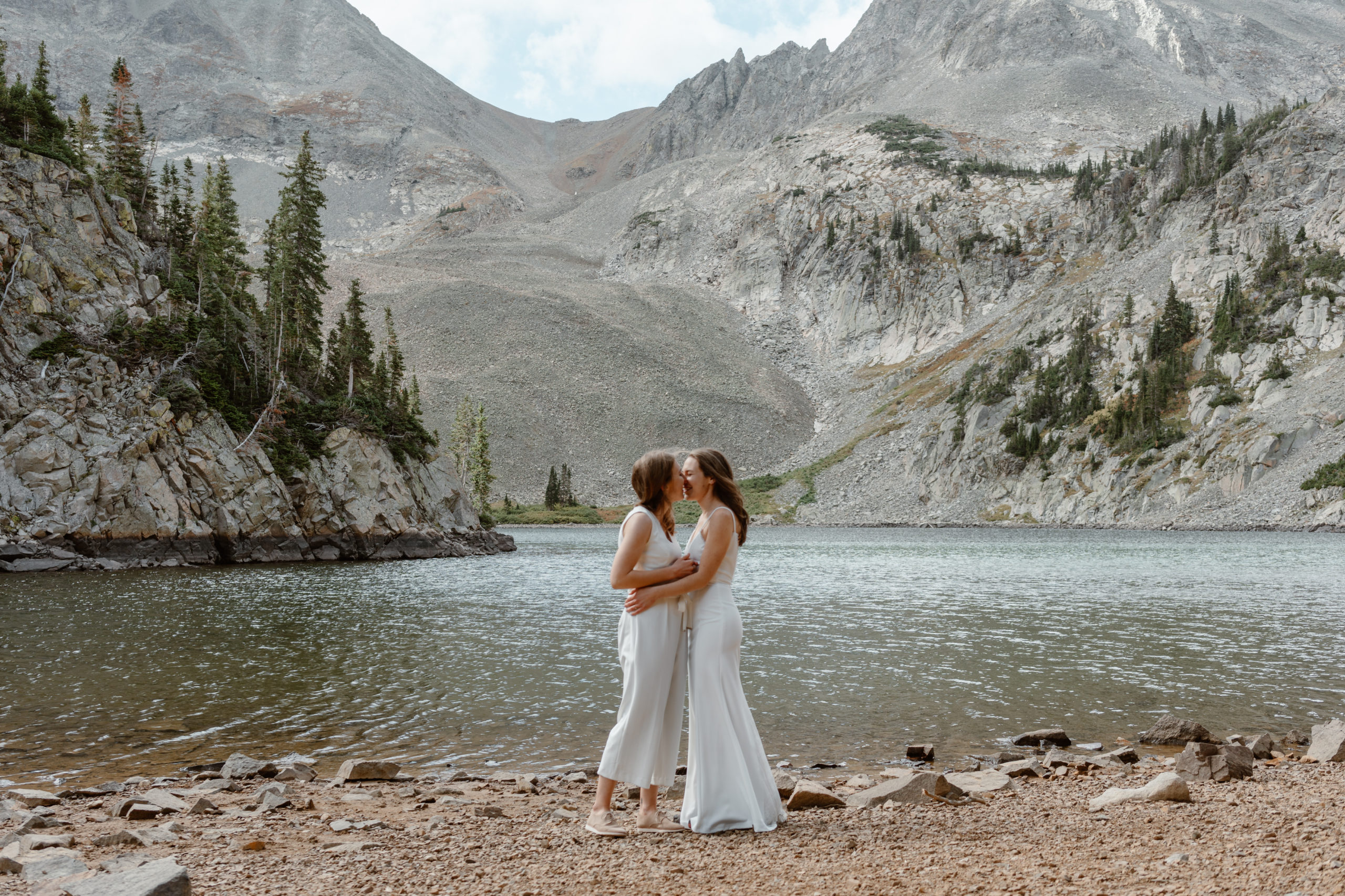 Two brides lean in close to kiss each other during their sunrise mountain elopement in Colorado.
