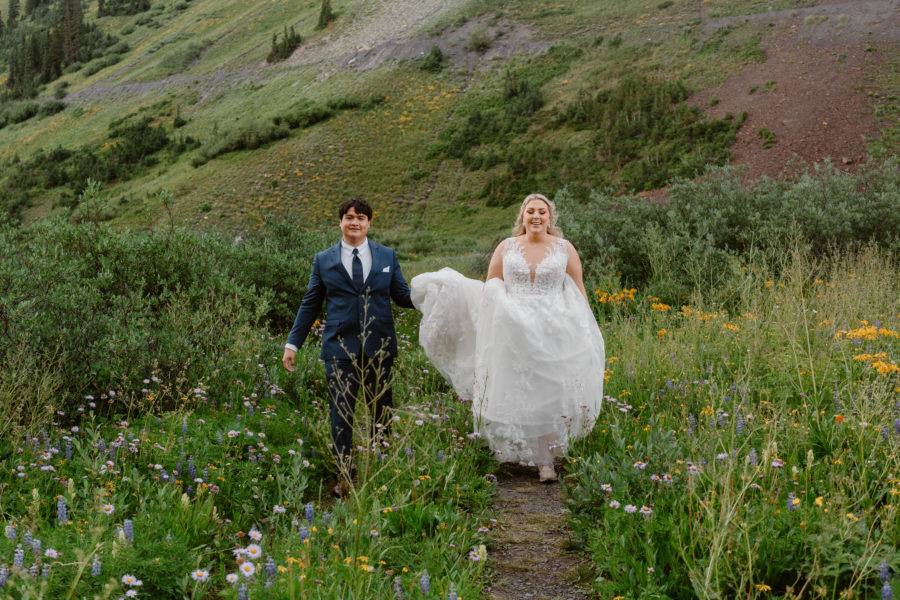 A bride and room run excitedly up a mountain trail during their summer Crested Butte elopement.