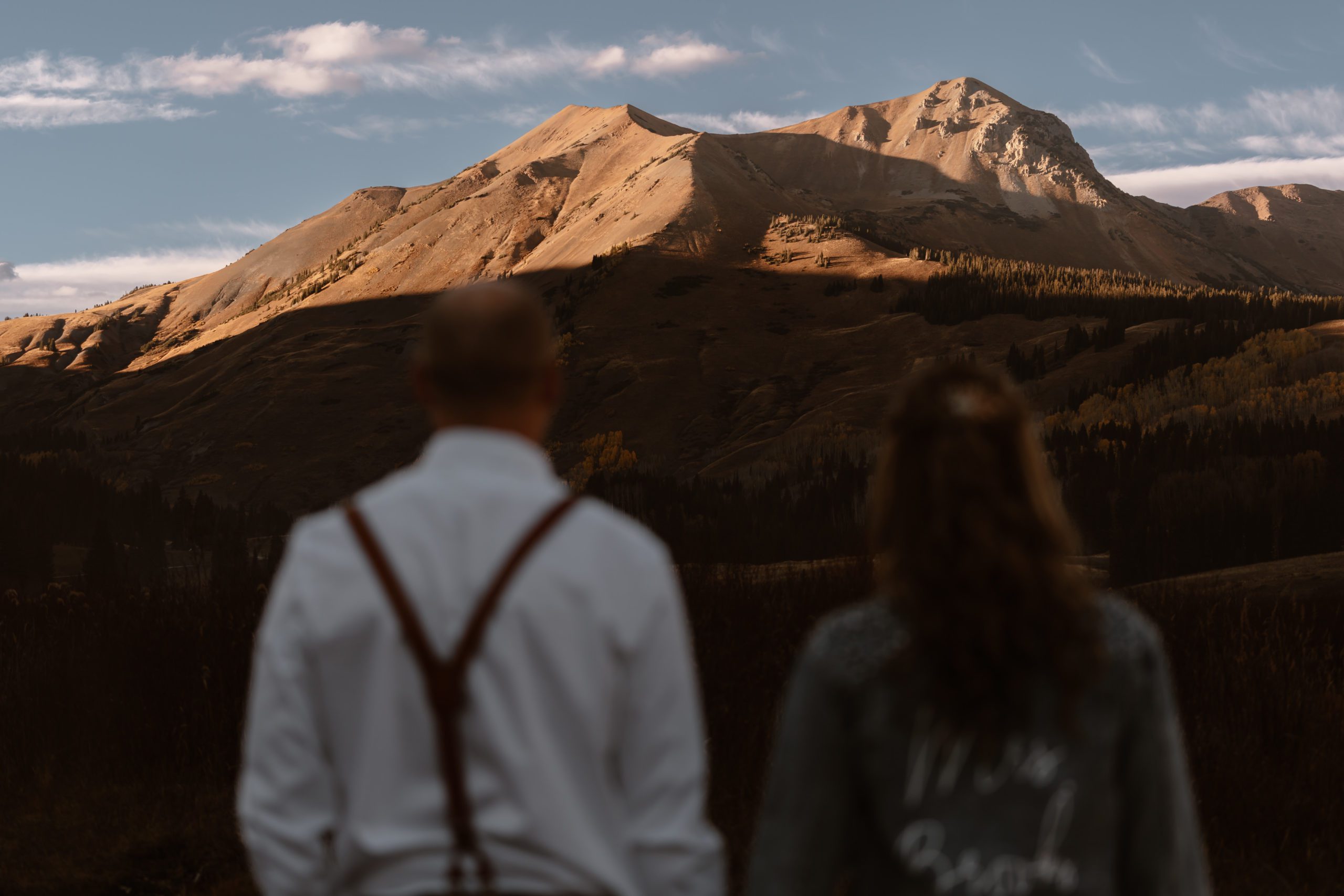 A bride and groom are shown in the blurry foreground with a focus on Mount Crested Butte in the background, sharper in focus, during their Crested Butte elopeent.