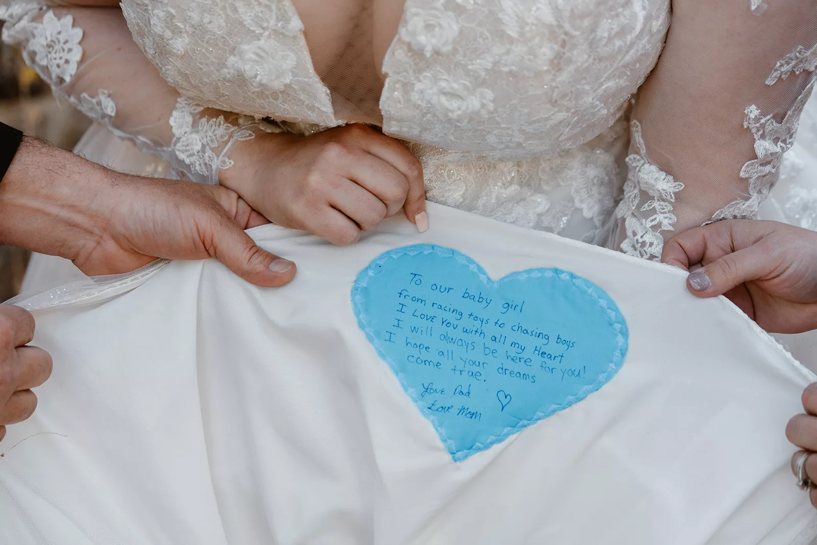 A bride shows off her unique note from her parents, hand stitched into her wedding dress 