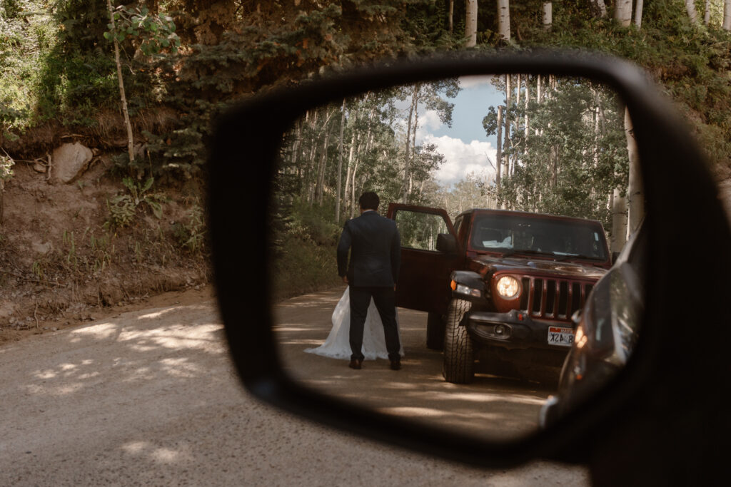 A bride and groom are shown in the rearview mirror of their 4x4 adventure vehicle wedding.