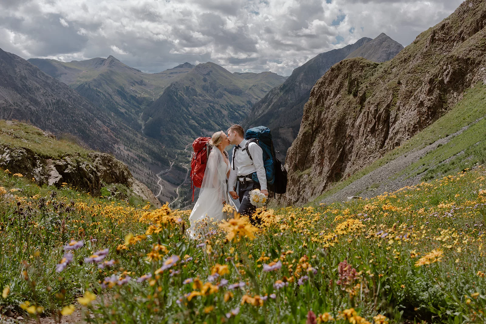 A couple poses in front of the wild yellow flowers in a mountain range during their San Juan mountain elopement.