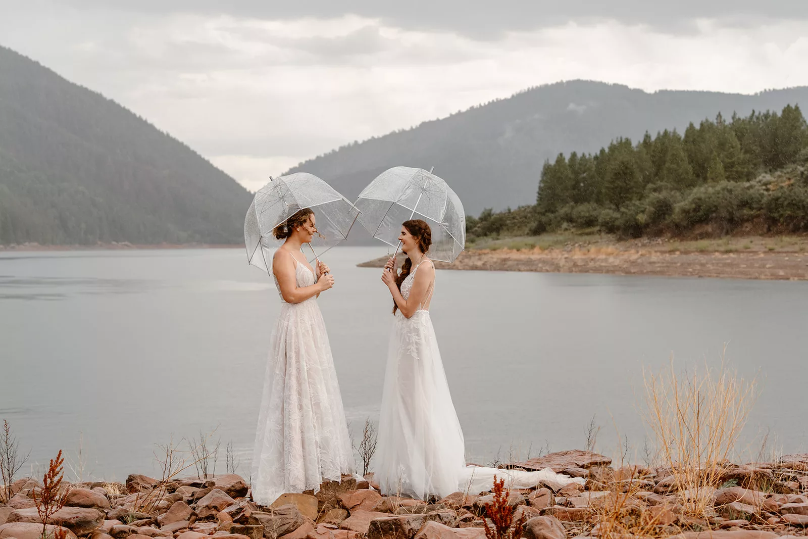 A couple huddles under umbrellas during their elopement day ceremony, proving that you can have fun even when the weather turns.