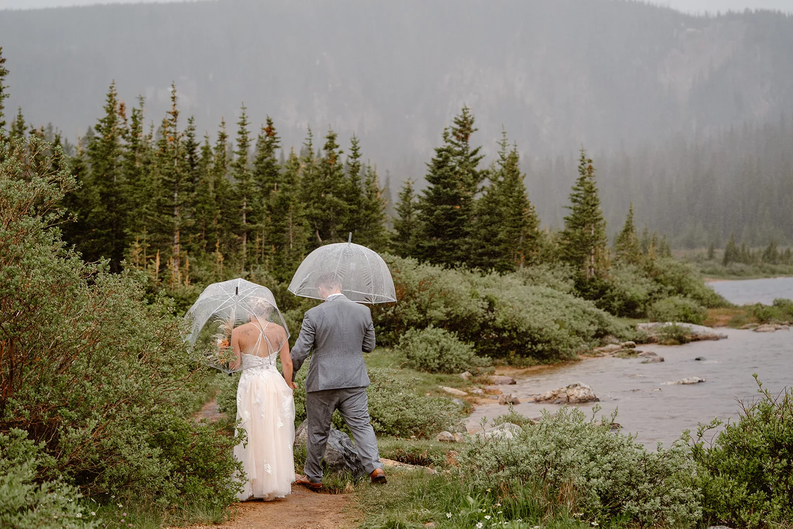 A husband and wife explore the Colorado wilderness together on their elopement day with see-through umbrellas. 