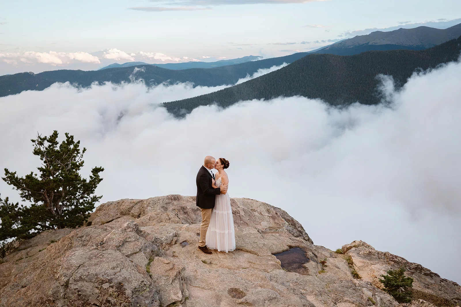 A couple kisses during their Colorado elopement on the top of a cloudy mountain vista.