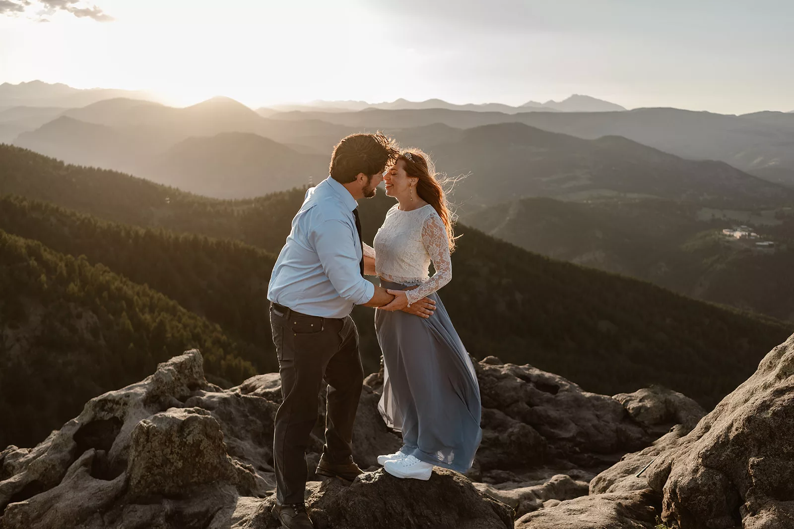 A man and woman lean in close on a mountain cliffside during golden hour during their engagement photoshoot.